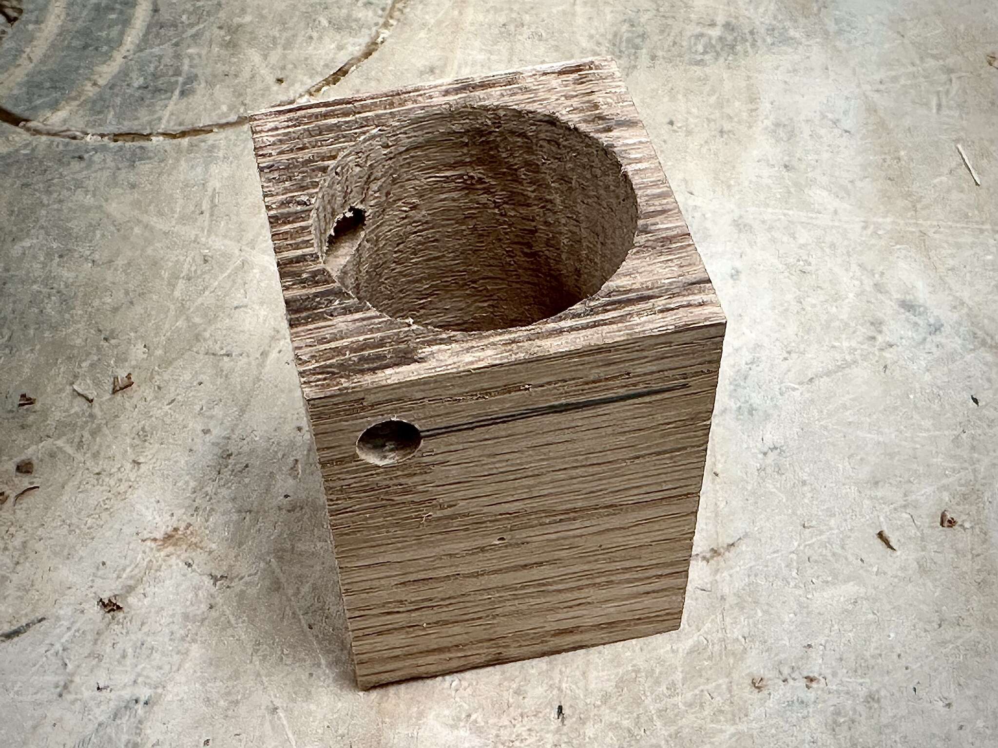 a tall cubic wood piece, with a big cylindrical hole at its center and a small hole on its side