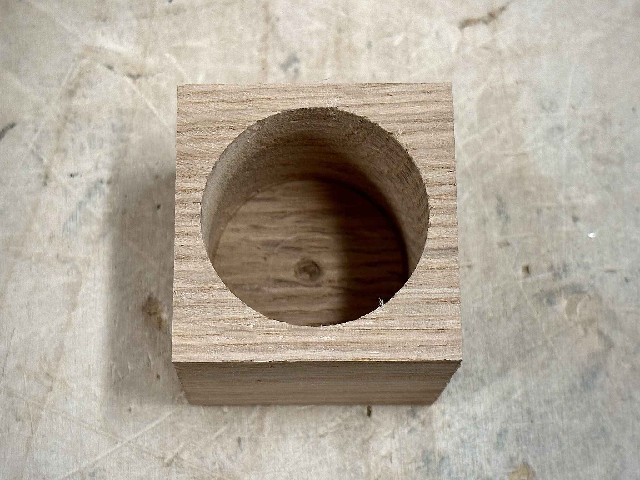 a slightly shorter cubic wood piece, with a big cylindrical hole at its center and top section already cut off
