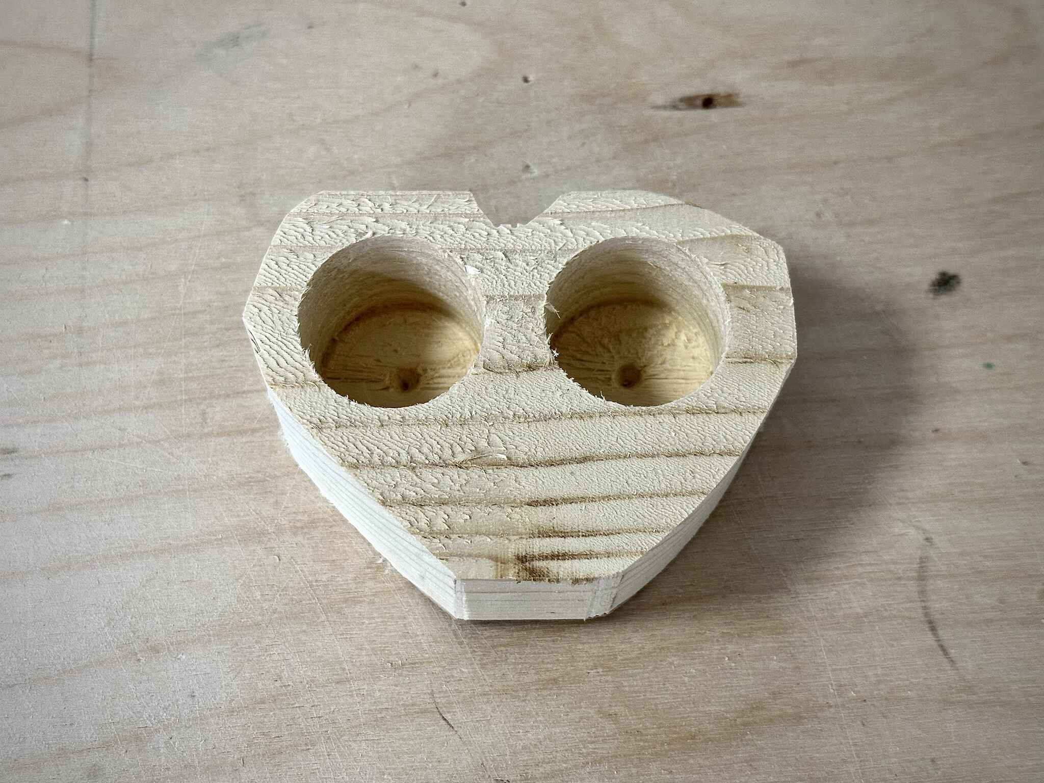 a roughly heart-shaped beige wood piece with two cylindrical holes